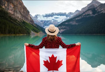 a woman standing in front of a lake holding a canadian flag