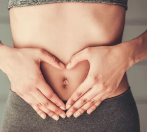 a woman forming her hands into the shape of a heart over her stomach