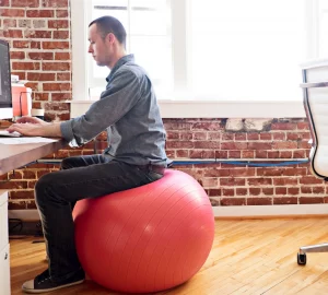 a man sitting on a mobility ball at a desk